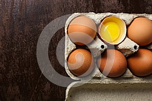 Fresh brown eggs and a broken egg with yolk in an eco tray made from recycled paper on a dark wooden background