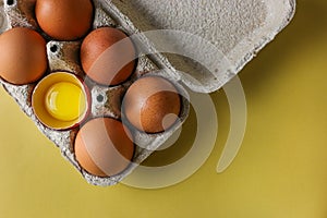 Fresh brown eggs and a broken egg with a yolk in a recycled paper eco tray on a light yellow background with space for text, copy