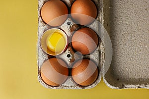 Fresh brown eggs and a broken egg with a yolk in a recycled paper eco tray on a light yellow background with space for text, copy
