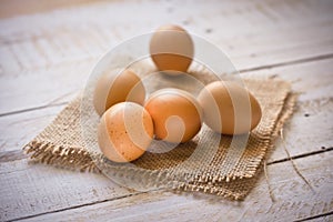 Fresh brown eggs on burlap cloth on white plank wood background, Easter, simplicity