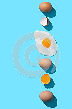 Fresh brown eggs, egg yolk and fried egg on blue background with copyspace. Vertical format