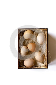 Fresh brown eggs and some straw in a wooden crate on a white background. Chicken eggs.