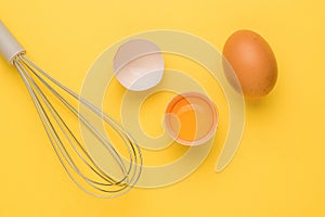 Fresh brown eggs and a whisk for whipping on a yellow background