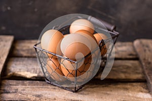 Fresh brown eggs in a wire basket on a vintage wood box, black background, Easter