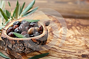 Fresh brown kalamata olives and leaves in olive wood bowl