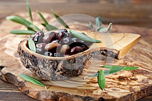 Fresh brown kalamata olives and leaves in olive wood bowl