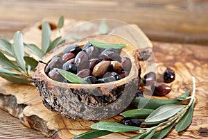 Fresh brown kalamata olives and leaves in olive wood bowl