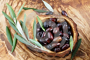 Fresh brown kalamata olives and leaves in olive wood bowl