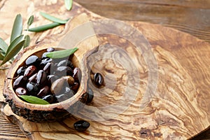 Fresh brown kalamata olives and leaves in olive wood bowl