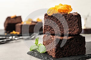 Fresh brownies decorated with orange peel and mint on table