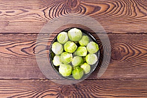 Fresh Brussels sprouts in a bowl on a black slate on a wooden table. Place for text