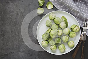 Fresh brussels sprouts in white plate isolated on dark background. Healthy vegan food, diet concept