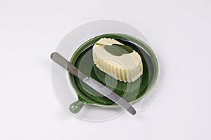 Fresh butter cube on ceramic dish with knife and green leaves of sage on white background.