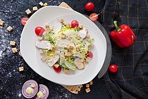 Fresh caesar salad with chicken on a white plate on dark stone background. Flat lay with ingridients for cook.
