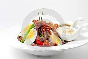 Fresh Caesar Salad with Deep-fried Bacon and Boiled Egg on White Porcelain Circle Dish, on White Background with Shadow. Close-Up