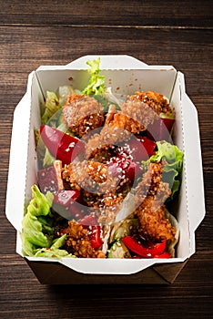 fresh caesar salad with fried chicken meat in paper take away container on wooden table