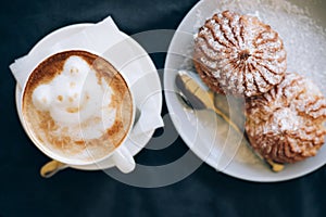 Fresh cappuccino art with plate with tasty cakes.