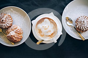 Fresh cappuccino art with two plates with tasty cakes.