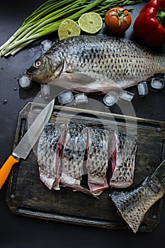 Fresh carp on a dark background with greens and vegetables. Cut into pieces carp on a wooden board