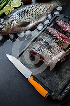 Fresh carp on a dark background with greens and vegetables. Cut into pieces carp on a wooden board