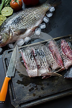 Fresh carp on a dark background with greens and vegetables. Cut into pieces carp on a wooden board