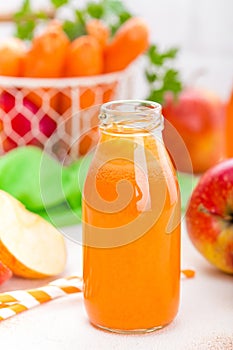 Fresh carrot and apple juice on white background. Carrot and apple juice in glass bottles on white table, closeup