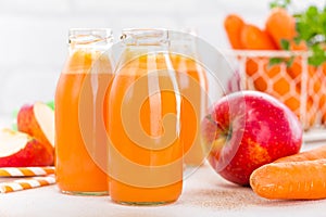 Fresh carrot and apple juice on white background. Carrot and apple juice in glass bottles on white table, closeup