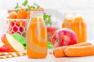 Fresh carrot and apple juice on white background. Carrot and apple juice in glass bottles on white table, closeup