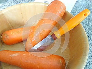 Fresh carrot and peeler in wooden bowl