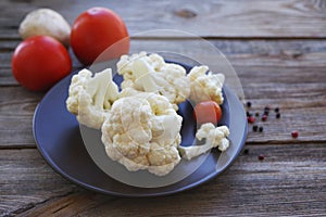Fresh cauliflower and cherry tomatoes on a brown round plate on a wooden surface