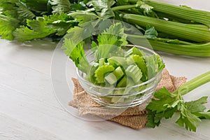Fresh celery sliced in bowl with bunch celery on white wood background