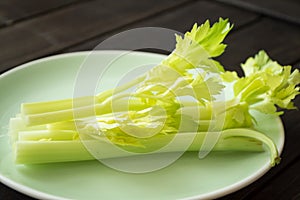 Fresh celery sticks on green plate and dark background