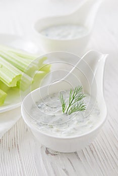 Fresh celery sticks with yogurt dip on white wooden background