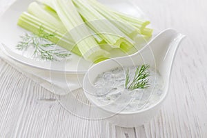 Fresh celery sticks with yogurt dip on white wooden background