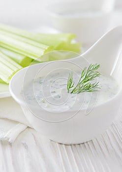 Fresh celery sticks with yogurt dip on white wooden background