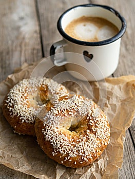 Fresh cheese donuts with sesame seeds on a wood background with metal white cup of coffee. Heathy food, diet, breakfast