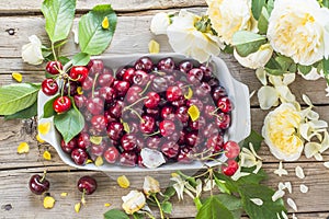 Fresh cherries in a bowl and roses on the wooden table