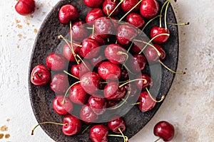 Fresh cherries close up in brown oval plate on white textured background, top view