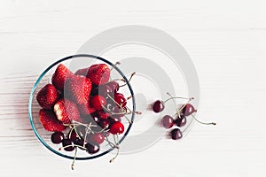 Fresh cherries and strawberries in stylish glass bowl on white r