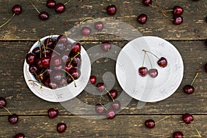 Fresh cherries in white vintage bowl on old wooden table. Ripe berries on background, summer day. Top view