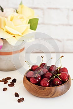 Fresh cherries in a wooden bamboo bowl. Bright Brick Wall Background. Yellow Roses in a Vase. Healthy Lifestyle Concept. Copy Spac