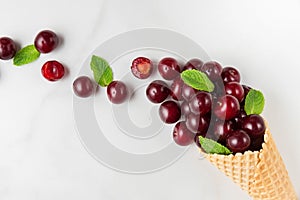 Fresh cherry berries with mint in waffle ice cream cone on white marble background. summer food concept. top view