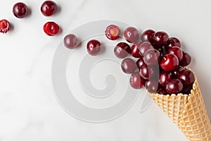 Fresh cherry berries in waffle ice cream cone on white marble background. summer food concept. top view