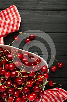 Fresh cherry in bowl with napkin on black background. Top view, copy space