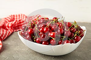 Fresh cherry in bowl with napkin on light background. Top view, copy space