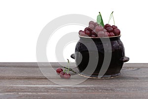 Fresh cherry in a pot on wooden table  isolated on white background