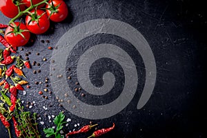 Fresh cherry tomatoes on a black background with spices with slate plate. Top view with copy space.