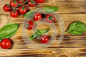 Fresh cherry tomatoes with green basil leaves on wooden table. Top view