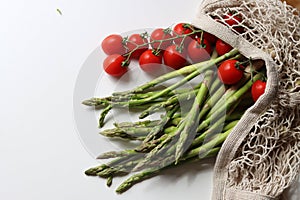 Fresh cherry tomatoes and green raw asparagus on white background with copy space. Vegetarian meal ingredients.