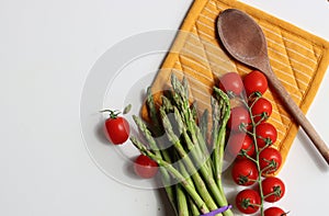 Fresh cherry tomatoes and green raw asparagus on white background with copy space. Vegetarian meal ingredients.